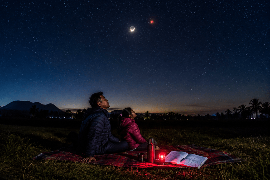 Pengamat langit mengamati konjungsi Bulan sabit dan Mars dengan mata telanjang di area terbuka bebas polusi cahaya.